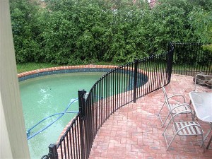 Curved black iron pool enclosure on a red brick patio beside a swimming pool
